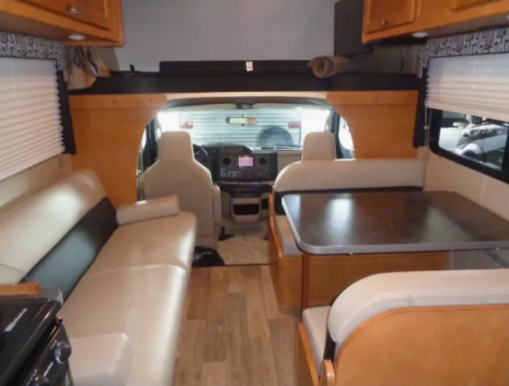 RV rental interior: light-toned dinette, lounge seating, partial kitchen, and cab-over bunk, offering comfort.. Winnebago Minnie Winnie 2019