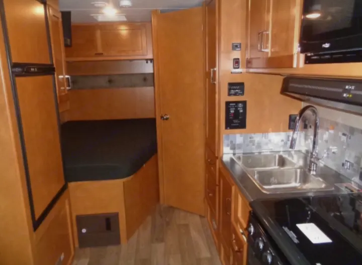 This RV rental interior has a functional kitchen with sink/stovetop, fridge, and a cozy bed area, all with light wood cabinetry.. Winnebago Minnie Winnie 2019