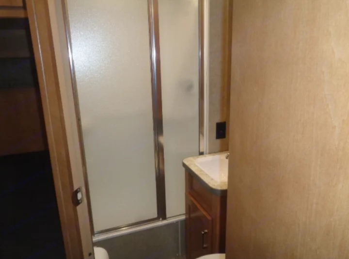 This RV rental's bathroom has a frosted glass shower, sink, and wood cabinetry, designed for compact living.. Winnebago Minnie Winnie 2019