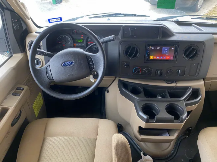 Interior view of an RV rental's dashboard and driver's seat with visible controls, infotainment, and cup holders.. Winnebago Minnie Winnie 2019
