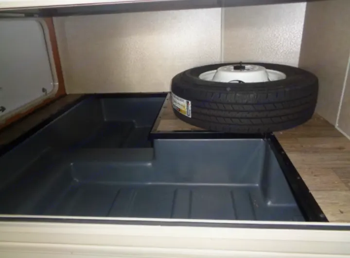 Built-in gray storage bins and a spare tire in an RV rental interior compartment.. Winnebago Minnie Winnie 2019