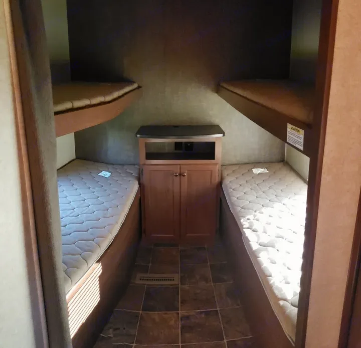 RV rental bunk bedroom featuring two sets of twin bunks, a central cabinet, and tiled flooring.. Heartland Prowler Lynx 2014