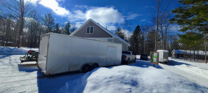 Large white enclosed trailer, suited for RV rental, with a snowmobile & truck at a snow-covered property.. Team spirit Enclosed 24-foot 2019