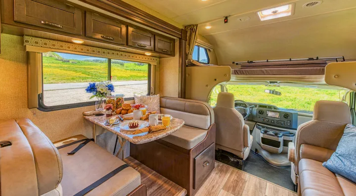 Bright RV rental interior: a comfy dinette set for breakfast by a large window, plus an overhead bunk.. Other Four Winds 2021