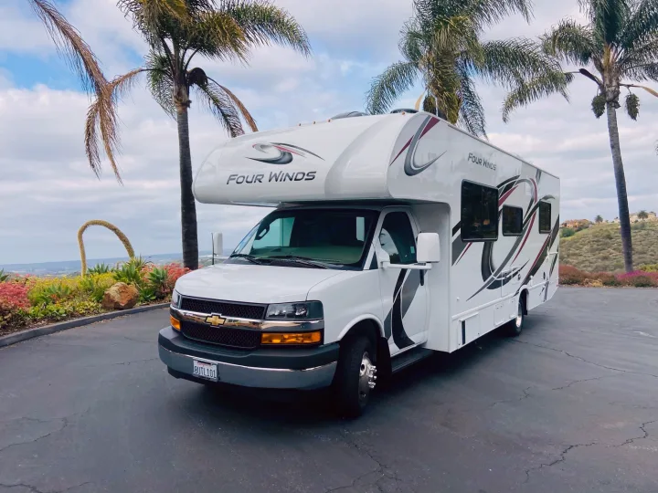 White Class C Four Winds RV rental parked under palm trees. Ideal for travel and scenic adventures with beautiful views.. Other Four Winds 2021