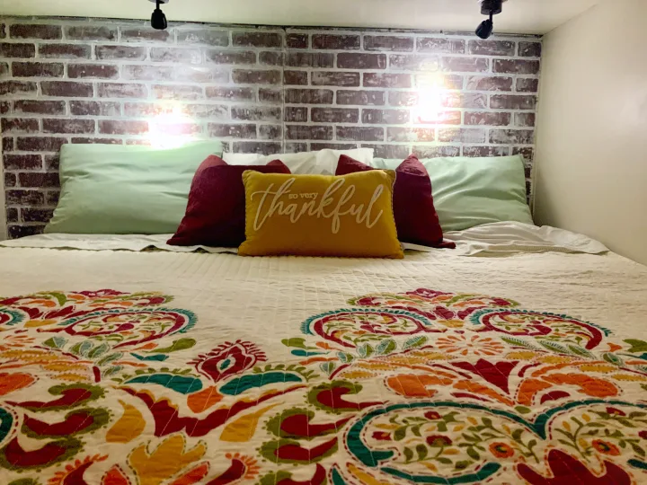 Cozy RV rental bedroom with a comfortable bed, colorful quilt, brick wall, and "thankful" pillow, ready for adventure.. Jayco Seneca 2013
