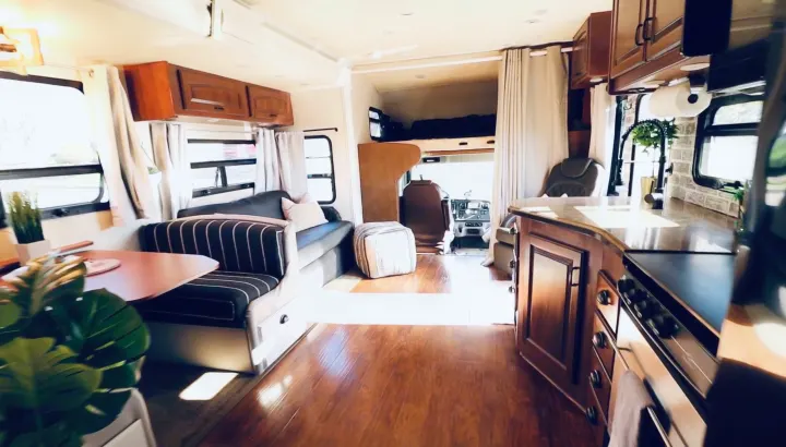 Cozy rv rental interior with dining, living, and kitchen areas, plus an overhead bunk & driver's cab.. Jayco Seneca 2013