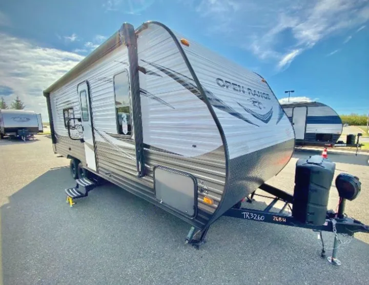 A grey Open Range travel trailer RV rental, parked outdoors under a blue sky, featuring an awning and steps.. Highland Ridge RV Open Range 2021