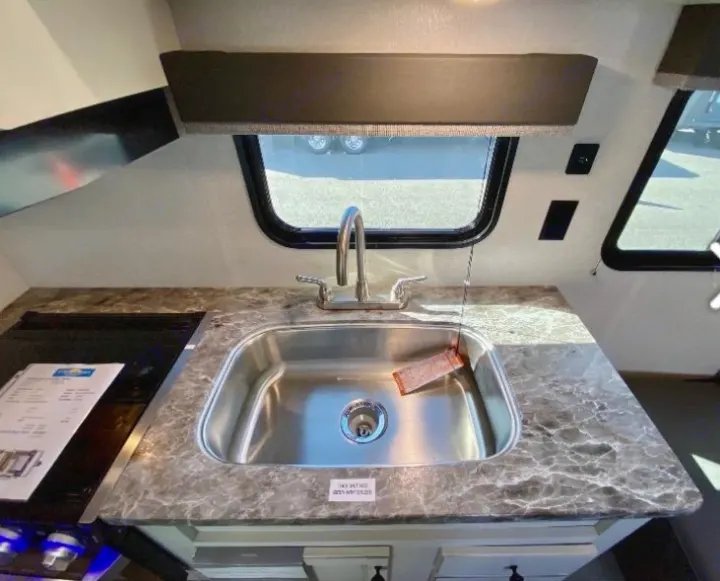 RV rental interior: A compact kitchen with a stainless steel sink, cooktop, and patterned countertop. Great for road trips.. Highland Ridge RV Open Range 2021