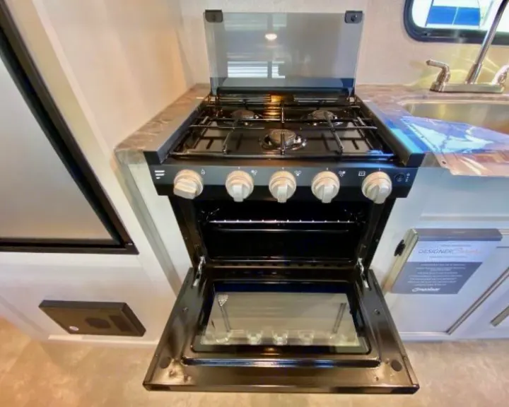 RV rental kitchen: Black gas range with 3 burners, glass cover up, and oven door open, next to a sink.. Highland Ridge RV Open Range 2021