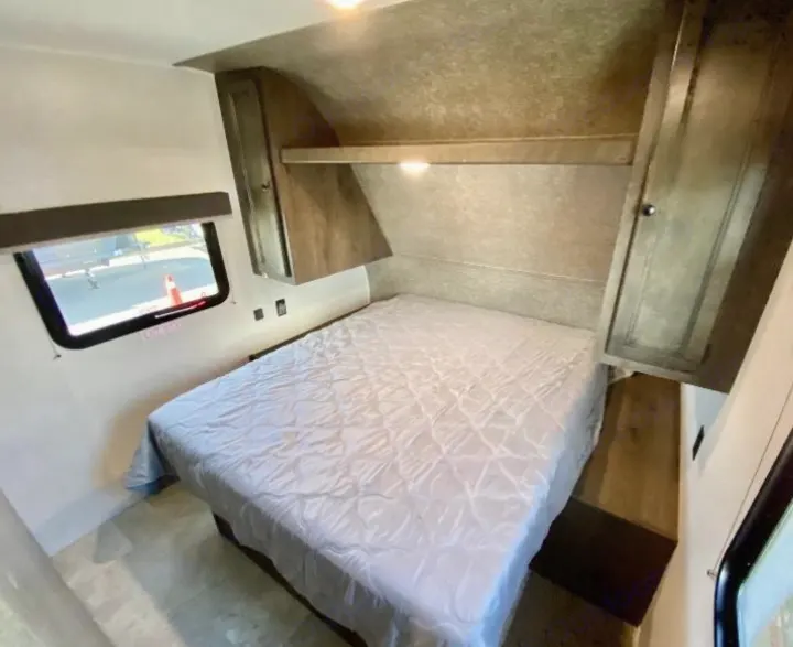 Inside an RV rental: a cozy bedroom with a large bed, window, and built-in shelving and cabinets.. Highland Ridge RV Open Range 2021