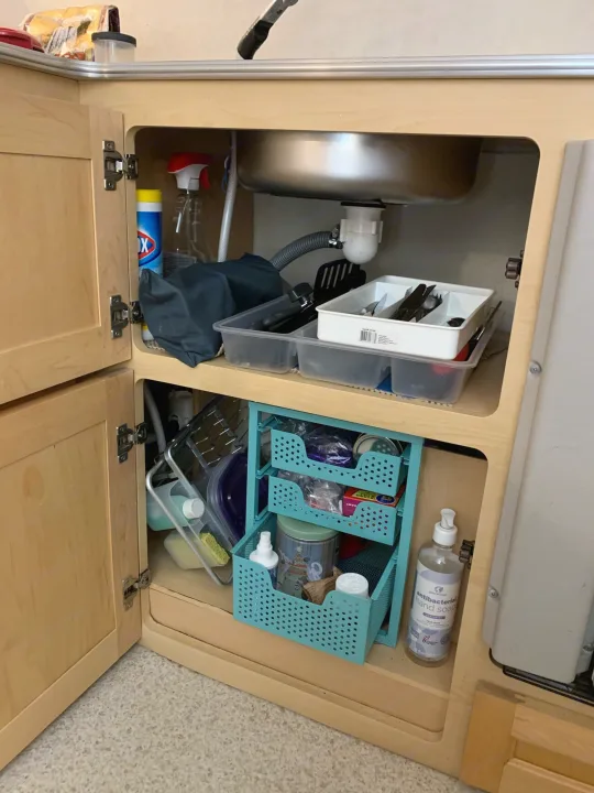 An RV rental's organized under-sink cabinet, showing cleaning supplies, kitchen utensils, and storage bins.. Dutchmen T@b 2008