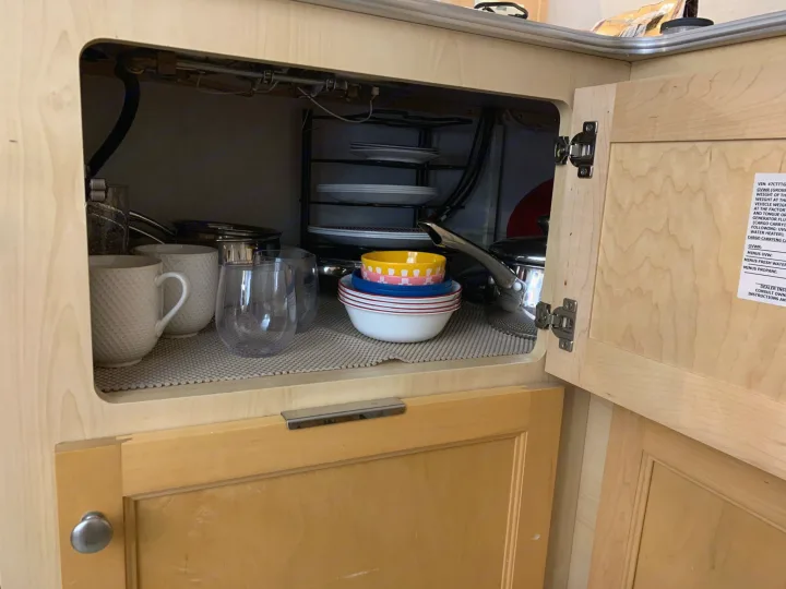 Inside an RV rental, a neatly organized kitchen cabinet holds dishes, bowls, cups, and pots for travel.. Dutchmen T@b 2008