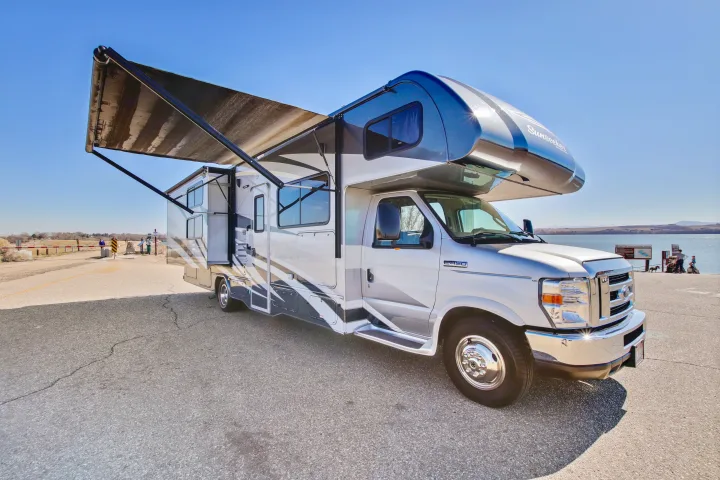 Spacious RV rental with awning extended, parked by a scenic lake. Perfect for outdoor adventures and travel in this motorhome.. Forest River Sunseeker 2018