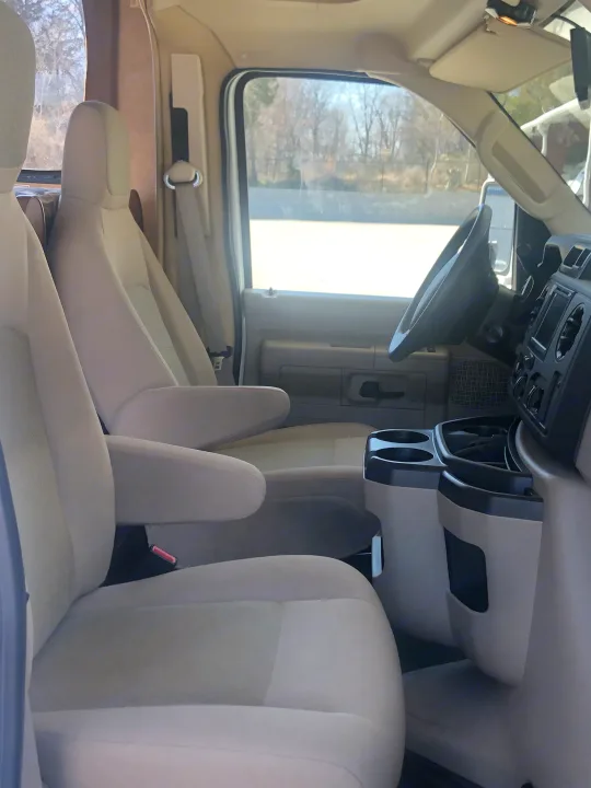 Spacious RV rental interior with comfortable, light beige seating. View from rear shows driver's area and passenger rows for travel.. Forest River Sunseeker 2014