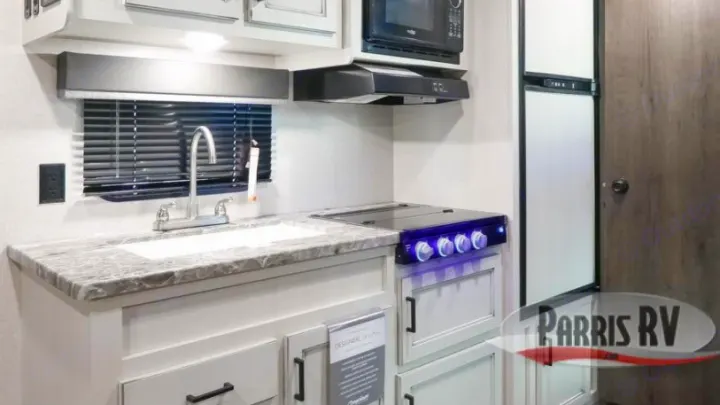 Well-equipped RV rental kitchen featuring a sink, modern stovetop, microwave, and refrigerator, ready for your travels.. Highland Ridge RV Open Range 2021