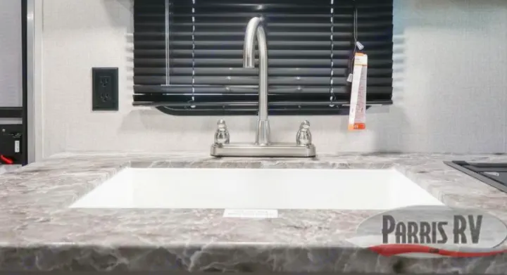 Modern RV kitchen featuring a stainless steel faucet, white sink, and patterned countertop. Perfect for your next RV rental trip.. Highland Ridge RV Open Range 2021