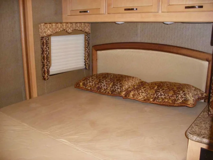 Cozy RV rental bedroom with patterned pillows, window, and overhead cabinets for a comfortable stay on the road.. Thor Motor Coach Freedom Elite 22FE 2017