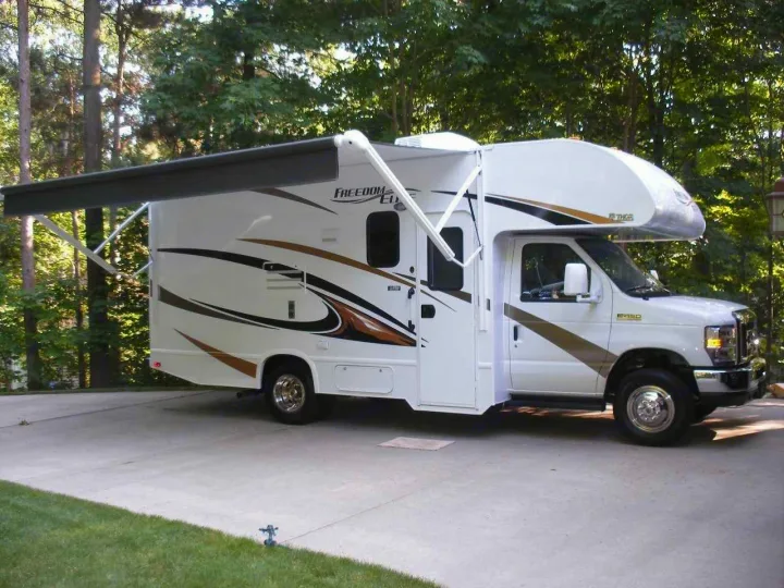 This white Class C RV rental, with its extended awning, is parked on a driveway, ready for a camping adventure.. Thor Motor Coach Freedom Elite 22FE 2017