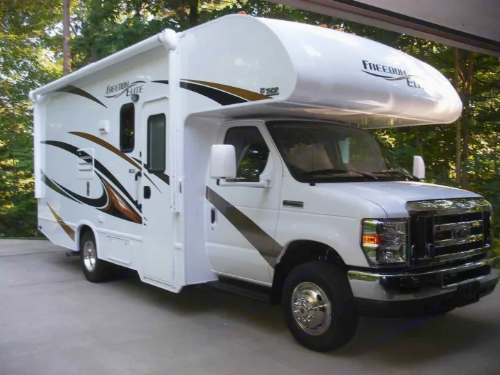 White Class C RV rental, "Freedom Elite" branded, featuring brown/black graphic decals. Parked among trees.. Thor Motor Coach Freedom Elite 22FE 2017