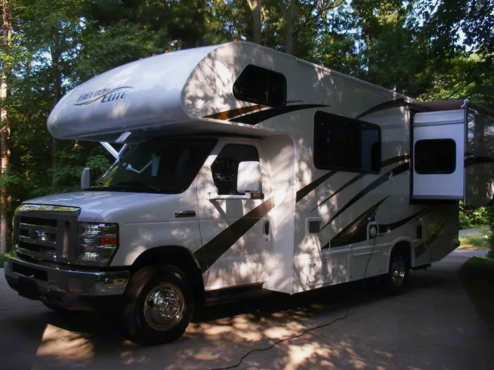 This spacious white and brown Freedom Elite motorhome, perfect for an RV rental, is parked outdoors with a slide-out extended.. Thor Motor Coach Freedom Elite 22FE 2017