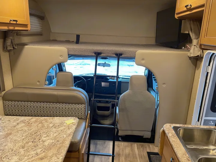 Inside an RV rental: view of the cab-over bed, cockpit, dinette, and kitchen. A ladder provides bunk access.. Thor Motor Coach Freedom Elite 22FE 2017