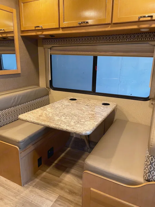 Spacious RV rental dinette featuring comfortable seating, a sturdy table with cupholders, large window, and ample wood cabinets.. Thor Motor Coach Freedom Elite 22FE 2017