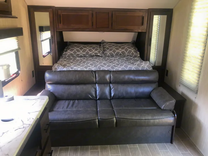 Comfortable RV rental interior with a cozy queen bed, overhead storage, and inviting sofa, ideal for your next adventure.. Forest River Cherokee Grey Wolf 22MKSE 2020