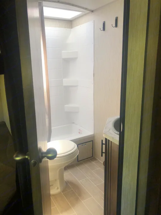 Compact RV rental bathroom features a clean toilet, shower/tub combo, and sink vanity with wall hooks.. Forest River Cherokee Grey Wolf 22MKSE 2020