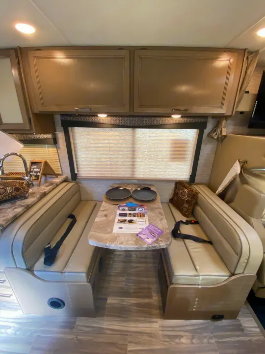 A modern RV rental interior, showing a comfortable dinette with cushioned benches, a table, and ample overhead storage.. Other Four Winds 2021