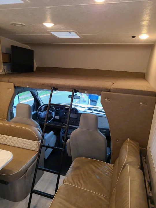 RV rental interior showing the large cab-over sleeping area with TV, ladder, and front cabin view.. Coachmen Freelander 2021