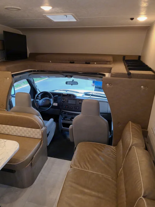 Spacious rv rental interior showing the cockpit, over-cab bunk with TV, dinette, and a comfy sofa.. Coachmen Freelander 2021