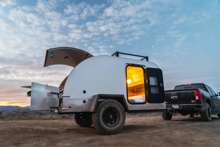 An RV rental teardrop camper, with its illuminated sleeping area and open rear kitchen, hitched to a pickup truck for off-grid camping.. PINNACLE Pinnacle Summit 2020