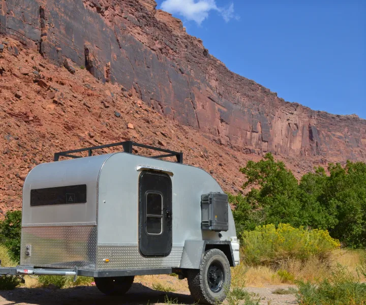 This rugged off-road camper trailer, ideal for an RV rental adventure, is parked against a huge red rock cliff.. PINNACLE Pinnacle Summit 2020