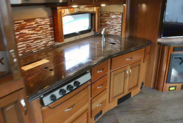 Experience comfort in this RV rental kitchen, featuring a dark countertop, stove, sink, and stylish wood cabinetry.. Fleetwood Pace Arrow 2018