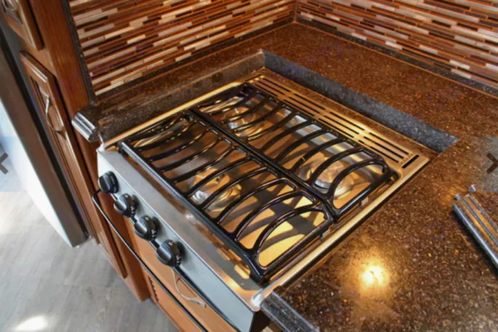 Modern RV rental kitchen featuring a four-burner stovetop, dark speckled countertops, and a stylish tile backsplash.. Fleetwood Pace Arrow 2018