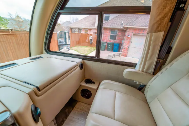 Spacious RV rental interior featuring a comfy passenger seat, console, and large window view of a residential backyard.. Thor Motor Coach Axis 2018