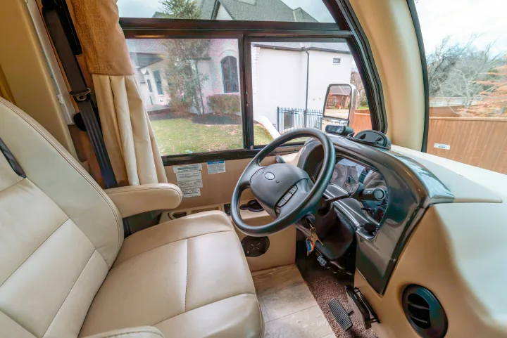 Explore the driver's cockpit of this RV rental, featuring a cream leather seat, Ford steering wheel, and clear views.. Thor Motor Coach Axis 2018