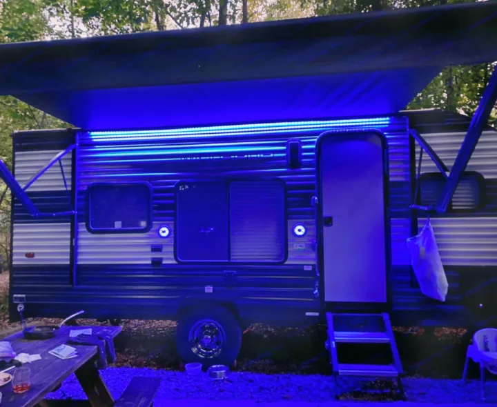An RV rental gleams under blue LED lights at a campsite, with a picnic table and high chair nearby, enhancing the evening ambiance.. Forest River Wolf Pup 2021