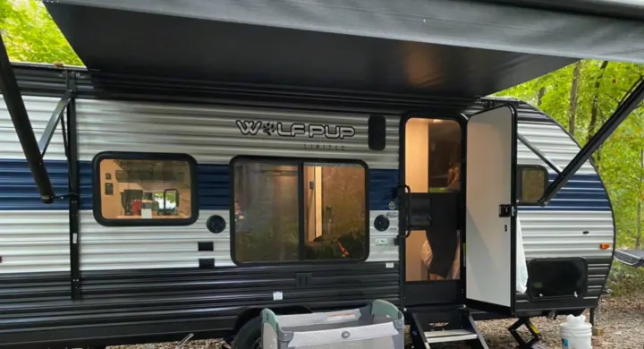 RV rental: A blue and gray Wolf Pup travel trailer with its awning out, door open, parked in a wooded campsite.. Forest River Wolf Pup 2021