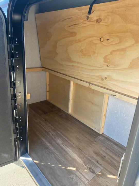 Inside an RV rental: a large, empty wood storage compartment with laminate flooring and an open door.. Forest River Wolf Pup 2021