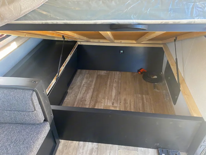 This RV rental features spacious under-bed storage, perfect for camping gear. The bed lifts to reveal a clean, wood-floored compartment.. Forest River Wolf Pup 2021