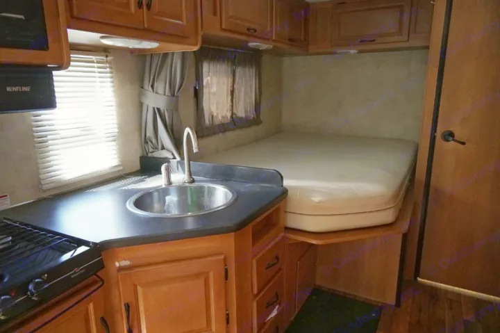 Inside this RV rental: a compact kitchen with sink and stove, plus a cozy bed area, ideal for mobile living.. Thor Motor Coach Four Winds Majestic 2013