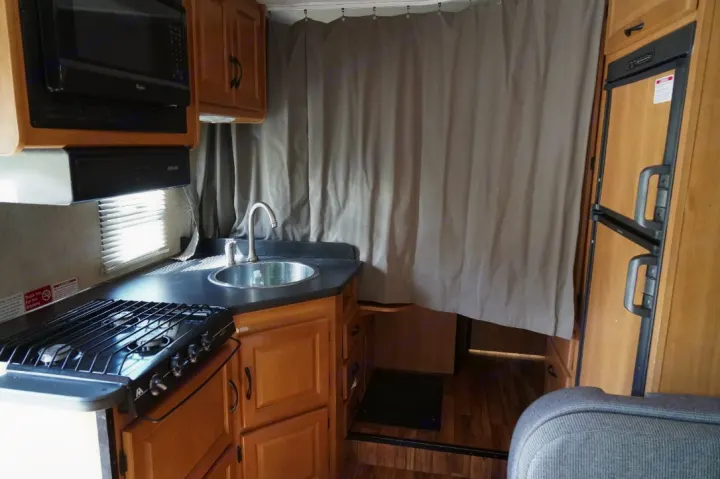 This RV rental kitchen shows a stovetop, microwave, sink, and fridge with wooden cabinets. Ideal for travel and camping adventures.. Thor Motor Coach Four Winds Majestic 2013