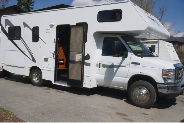 White RV rental, a Class C motorhome, parked on asphalt with its side door open. Ready for adventure!. Thor Motor Coach Four Winds Majestic 2013