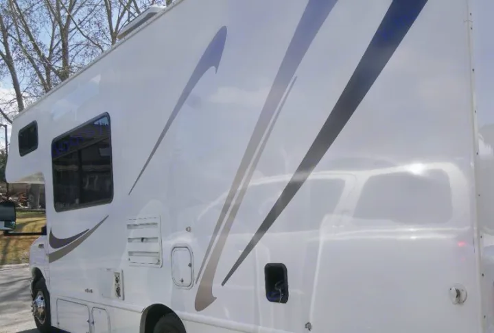 Side view of a gleaming white RV rental with gray graphic stripes, windows, and utility panels. Perfect for your travel adventures.. Thor Motor Coach Four Winds Majestic 2013