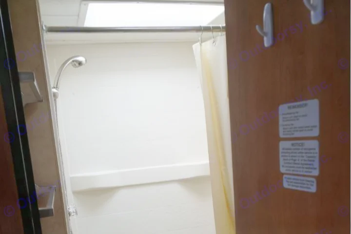 RV rental interior: A compact white shower with a shower head, curtain, and hooks on the adjacent door, designed for travel.. Thor Motor Coach Four Winds Majestic 2013
