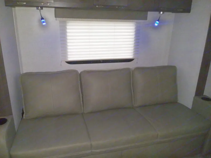 Cozy RV rental interior showing a three-cushion sofa, window with pleated blinds, and accent LED lights.. Forest River Rockwood Mini Lite 2021