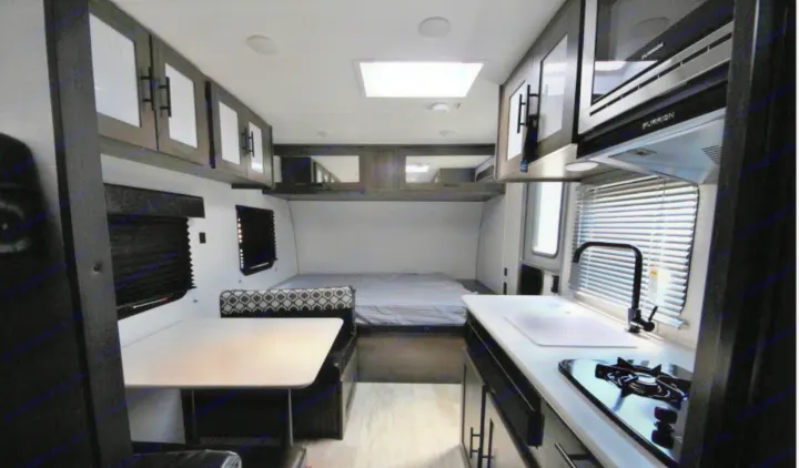 RV rental interior: Kitchen with sink, stovetop, microwave, overhead cabinets. Dinette and bed area. Modern design.. Prime Time Avenger 2021