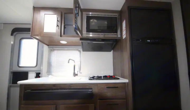 Explore this rv rental kitchen featuring a microwave, stove, sink, large refrigerator, and dark wood cabinets.. Prime Time Avenger 2021